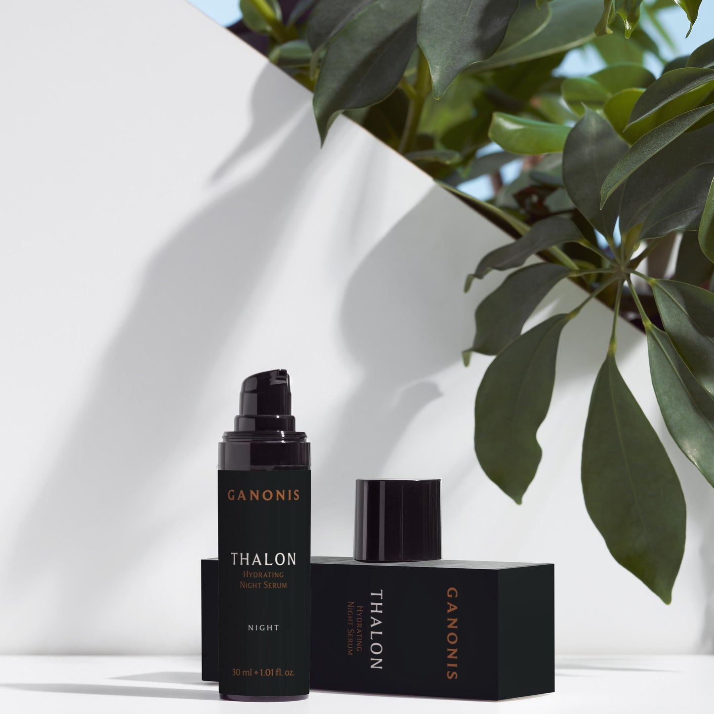 One black cosmetic bottles with THALON by GANONIS branding and its packaging on a white surface with green leaves in the background.